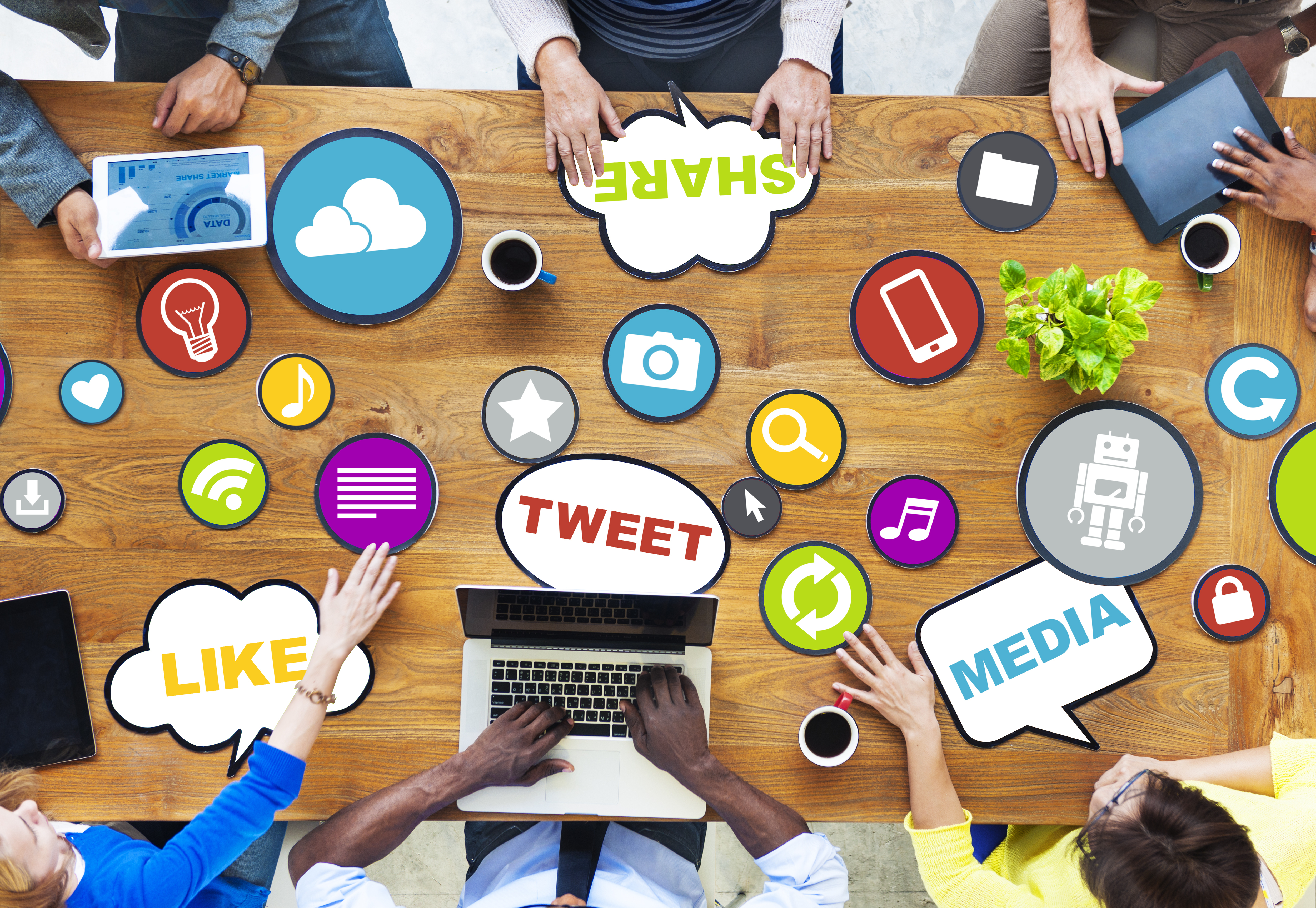 A group of hands working on a desk with speech bubbles that describe different social media lingo such as tweet, like, and share